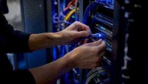 Persons hands connecting a blue Ethernet cable to a server rack in a data center